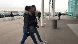Pareja caminando frente a la entrada de un edificio con fachada de vidrio 2oCpfEU8HFc.