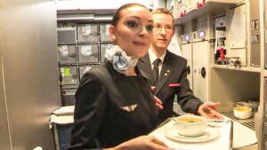 Tripulante de cabina con uniforme y otro miembro de la tripulación entregando un plato de sopa en la galley del avión iucjHkYPuG8.