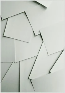 Planificadores digitales vs planificadores de papel: pros y contras que debes conocer, imagen de hojas de papel blancas superpuestas en ángulos geométricos que evoca planificación en papel