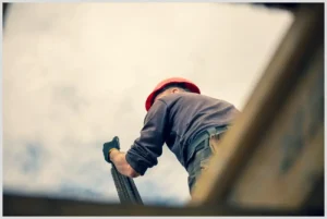Obrero con casco rojo y guantes sosteniendo una barra de acero visto desde abajo, Teletrabajo 3 días a la semana: Mejora tu productividad y calidad de vida ahora mismo