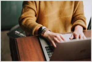 Manos escribiendo en un portátil sobre una mesa en un entorno de trabajo desde casa, Teletrabajo falta de comunicación: Cómo superar los obstáculos y mejorar la conexión en equipos remotos