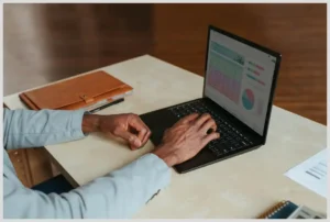 Teletrabajo y la gestión del cambio: Claves para transformar tu productividad ahora mismo, manos trabajando en un portátil con gráficos y documentos sobre una mesa.