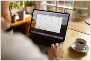 Teletrabajo con niños pequeños en casa: Consejos para la convivencia y productividad familiar, persona usando un portátil con gráficos en una mesa de madera junto a una taza de café